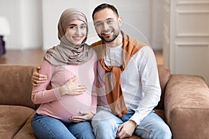 Happy Muslim Husband Hugging Pregnant Wife Sitting At Home