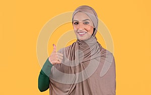 Happy Muslim Lady In Hijab Gesturing Thumbs-Up Over Yellow Background