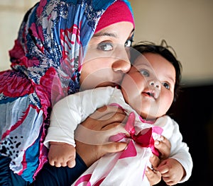 Happy, muslim and mom kiss baby in portrait at home with love and care for family in Saudi Arabia. Infant, child and