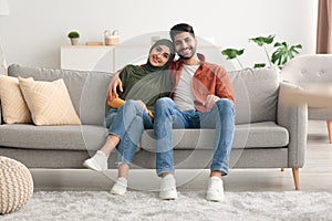 Happy Muslim Spouses Sitting On Sofa Embracing Posing At Home