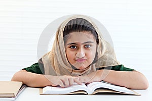 Happy Muslim student girl with beautiful eyes wears hijab traditional costume, study and do homework on table, kid read book on