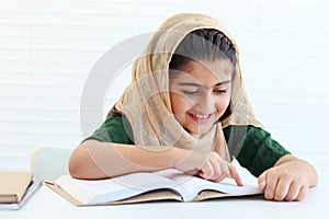 Happy Muslim student girl with beautiful eyes wears hijab traditional costume, study and do homework on table, kid read book on