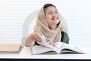 Happy Muslim student girl with beautiful eyes wears hijab traditional costume, study and do homework on table, kid read book on