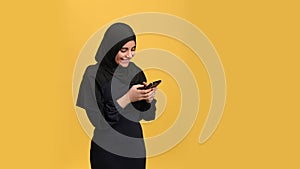 Happy Muslim woman in black hijab received good news lucky message use smartphone isolated on orange