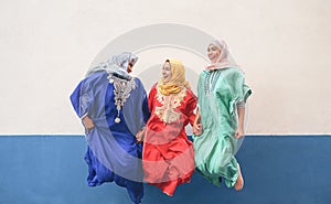 Happy Muslim women having fun jumping and laughing together outdoor - People lifestyle and culture religion concept