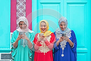 Happy muslim women using their mobile smart phones in the college - Arabian young people watching on cellphone and laughing