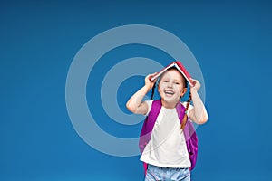 Happy, naughty little schoolgirl with a backpack, holding a book on her head