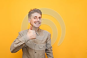 Happy nerd with mustache and glasses shows thumb up and looks into camera with happy face on yellow background. Geek in glasses