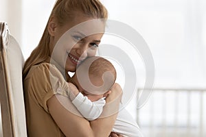 Happy new mom hugging and holding sleepy baby in arms