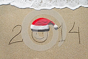 Happy new year 2014 with smiley face in christmas hat on sandy b