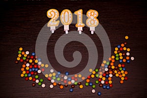 Happy new year 2018 text from candles with colorful candies on wooden background