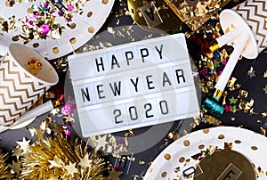 Happy new year 2020 on light box with party cup,party blower,tinsel,confetti.Fun Celebrate holiday party time table top view