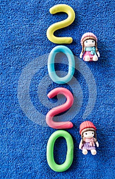 Happy New Year 2020 , molding of color clay with little girls toys on blue background.