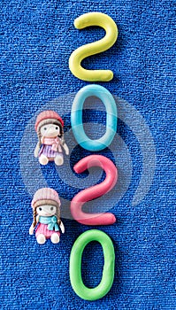 Happy New Year 2020 , molding of color clay with little girls toys on blue background.