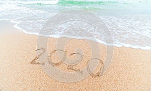 Happy New Year 2020 written on seashore sand at sunrise concept.beautiful sandy beach and soft blue ocean wave