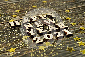 Happy New year 2021 celebration. Wooden text on wooden background with scattered golden confetti