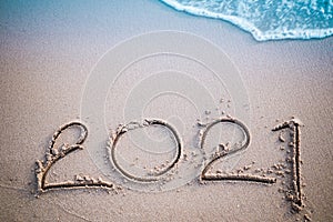 Happy New Year 2021 concept, 2021 number lettering on the sea beach, wave and golden light of sunset