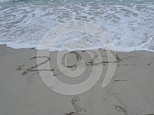 Happy New Year 2021, lettering on the beach with wave and clear blue sea.