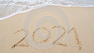 Happy New Year 2021 Text on the beach, 2021 year message hand written in sand on beautiful beach Waves crashing on sandy shore