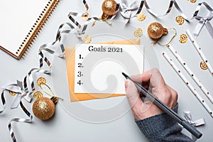 Happy New Year 2021. Woman`s hand writing in notebook decorated with Christmas decorations on the grey background. Top view, flat