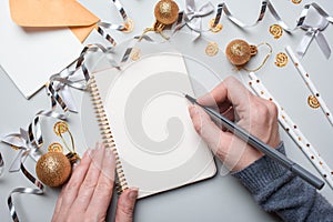 Happy New Year 2021. Woman`s hand writing in notebook decorated with Christmas decorations on the grey background. Top view, flat