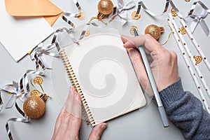 Happy New Year 2021. Woman`s hand writing in notebook decorated with Christmas decorations on the grey background. Top view, flat