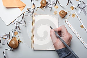 Happy New Year 2021. Woman`s hand writing in notebook decorated with Christmas decorations on the grey background. Top view, flat