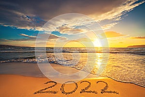 Happy New Year 2022 concept, lettering on the beach sand. Sea sunrise.