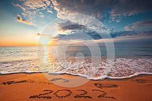 Happy New Year 2022 concept, lettering on the beach. Written text and footsteps on the sea sand at sunrise