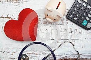 Happy New Year 2022 for healthcare and medical with piggy bank, stethoscope and calculator on wooden background
