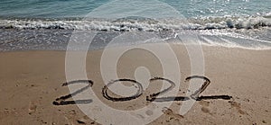 Happy New Year 2022, lettering on the beach with wave and clear blue sea.