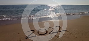 Happy New Year 2022, lettering on the beach with wave and clear blue sea.