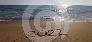 Happy New Year 2022, lettering on the beach with wave and clear blue sea.