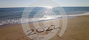 Happy New Year 2022, lettering on the beach with wave and clear blue sea.