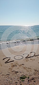 Happy New Year 2022, lettering on the beach with wave and clear blue sea.
