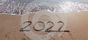 Happy New Year 2022, lettering on the beach with wave and clear blue sea.