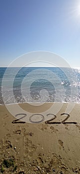 Happy New Year 2022, lettering on the beach with wave and clear blue sea.