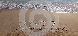 Happy New Year 2022, lettering on the beach with wave and clear blue sea.