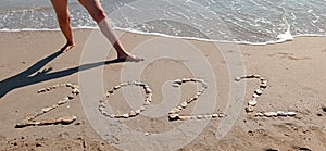 Happy New Year 2022, lettering on the beach with wave and clear blue sea.