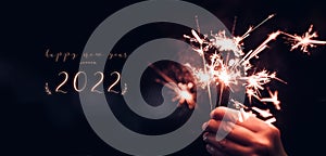 Happy new year 2022 text with hand holding burning Sparkler firework blast with on a black bokeh background at night,holiday