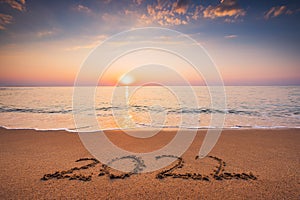 Happy New Year 2022 text, lettering on the beach sand. Sea sunrise.