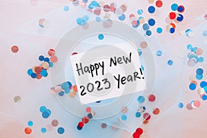 Happy new year 2023 - card with text and colorful confetti decorations on light blue textile background