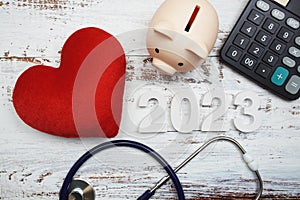 Happy New Year 2023 for healthcare and medical with piggy bank, stethoscope and calculator on wooden background