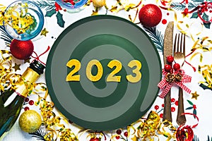 Happy new year 2023. Top view of golden Numbers 2023 on plate for Christmas dinner with christmas ornament and champagne bottle .