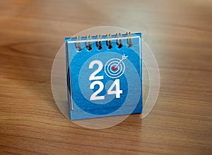 Happy new year 2024 background. 2024 numbers year with target icon as a zero number position on blue small desk calendar.