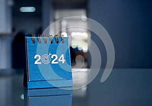 Happy new year 2024 background. 2024 year numbers with target goal icon on blue small desk calendar.