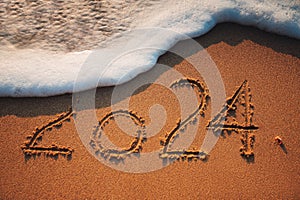 Happy New Year 2024 concept, lettering on the beach sand and splashing wave as nature background