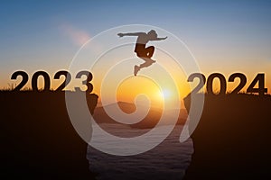 Happy new year 2024 concept. Silhouette of man jump on the cliff between 2023 to 2024 years over sunset or sunrise background