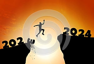 Happy new year 2024. Man silhouette jumping cliff from 2023 to 2024 on cloud sky background