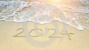 happy new year 2024. number 2024 write on sandy beach with ripple ocean wave splash with white bubble. countdown for happy new